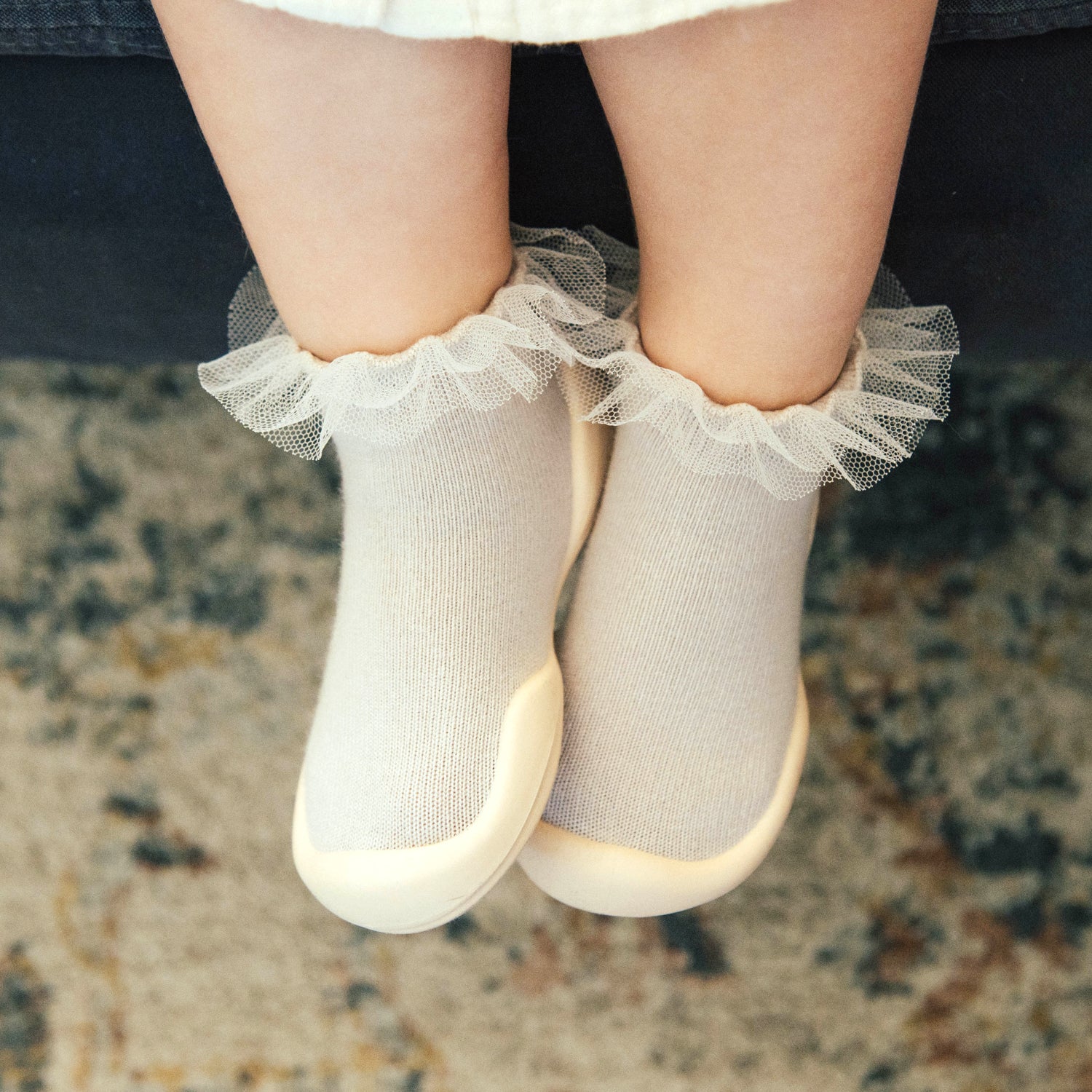 Baby's feet in white socks with frilly trim and shoe bottoms.