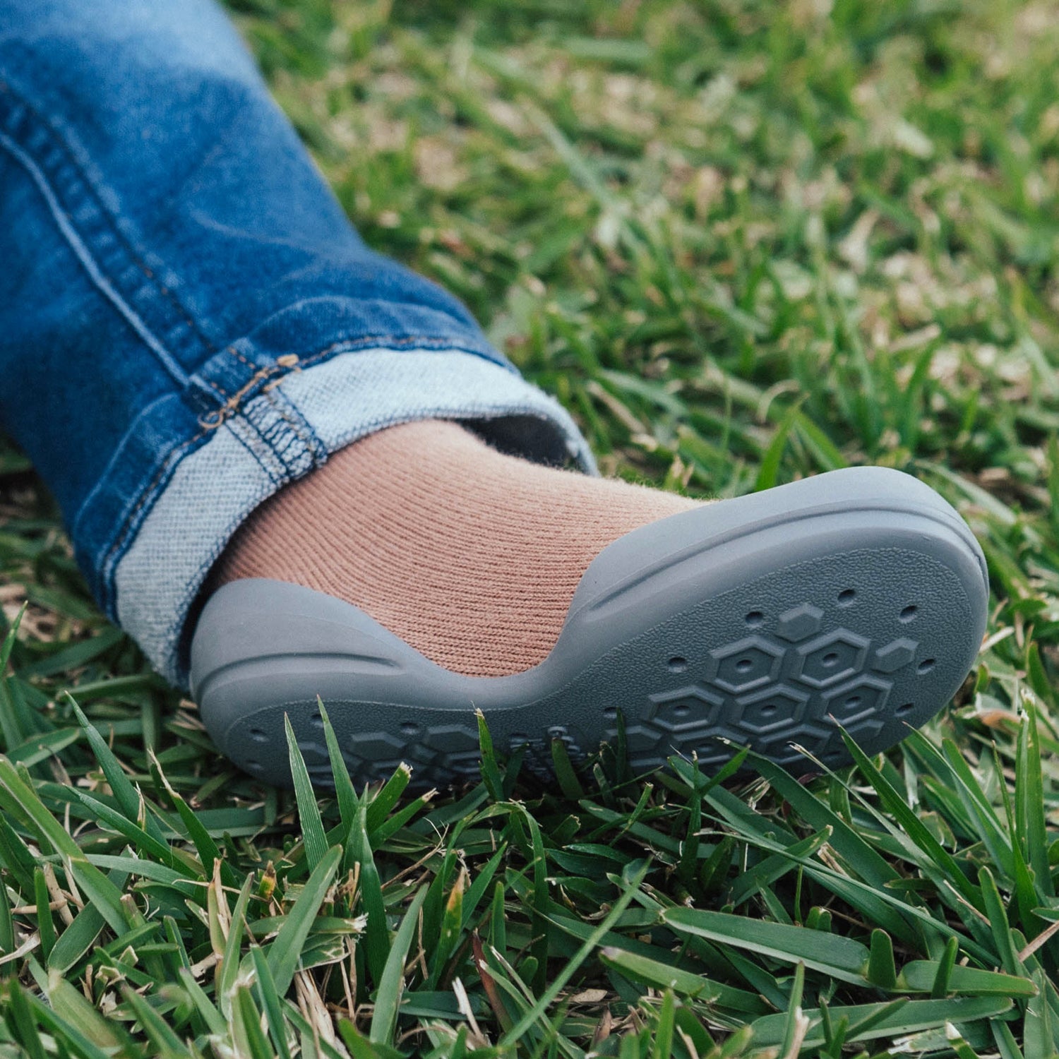 Leg wearing blue jeans, brown sock, and gray shoe on grass.