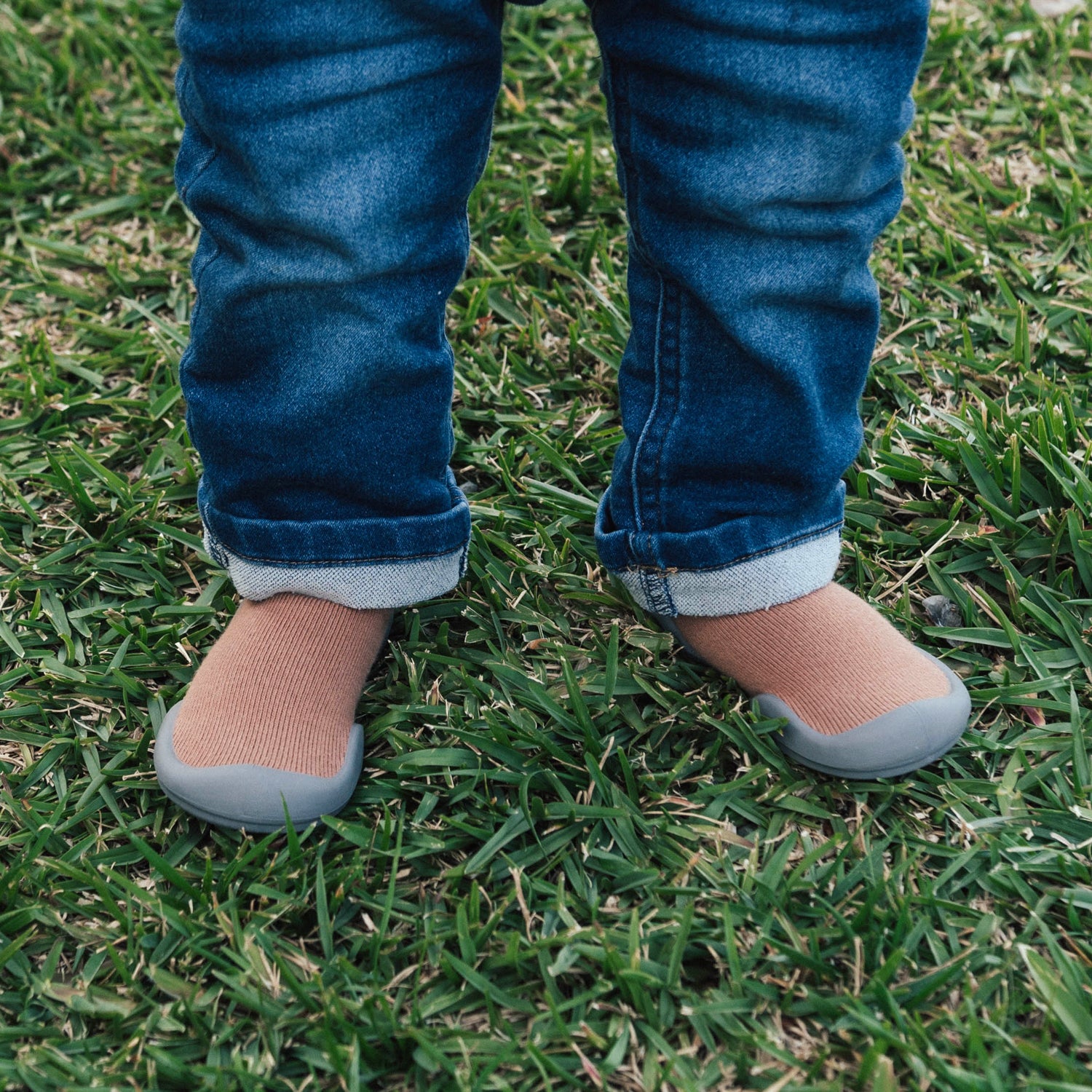 Child's legs in jeans and soft shoes on grass.