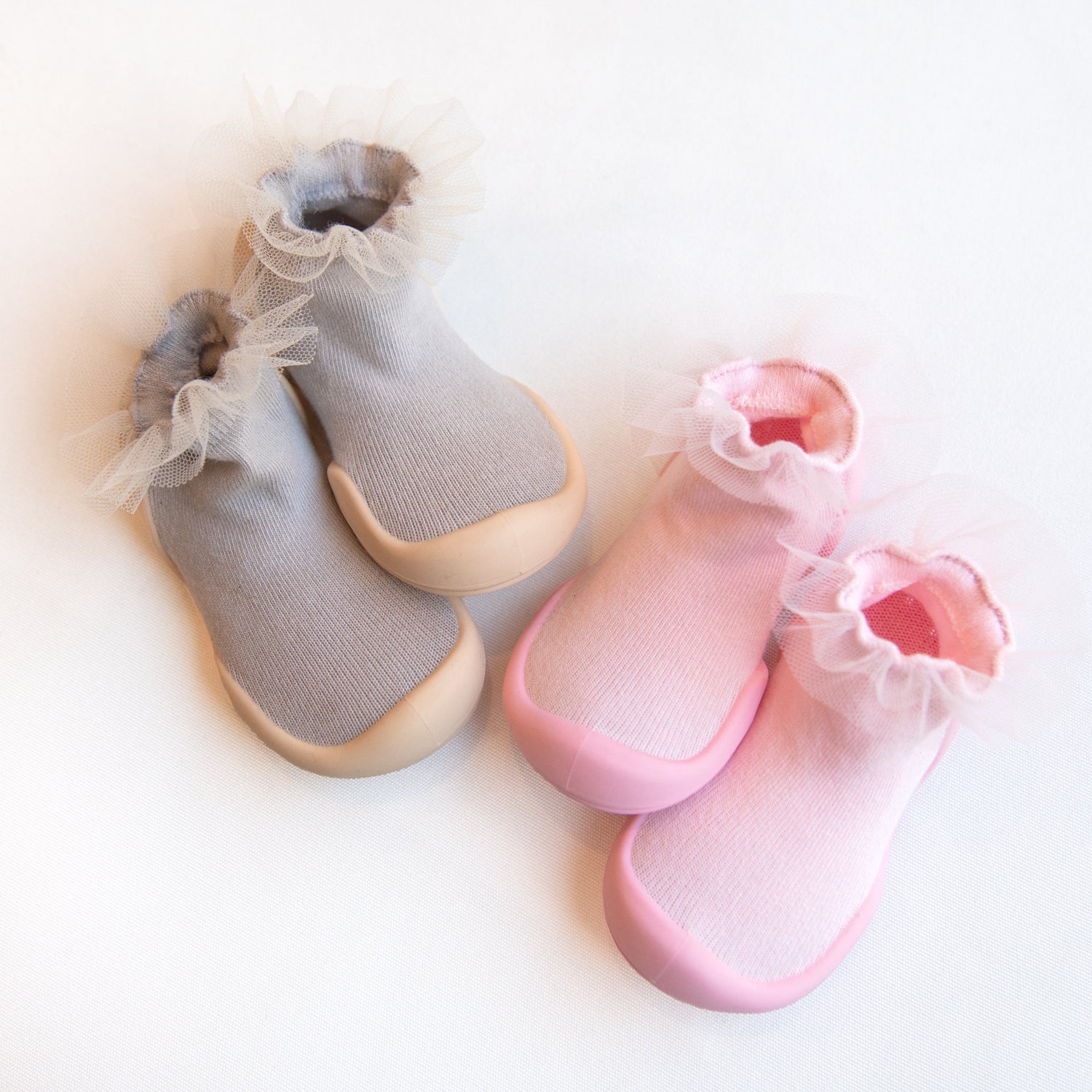 Two pairs of baby shoes in pink and gray with tulle trim on a white background.