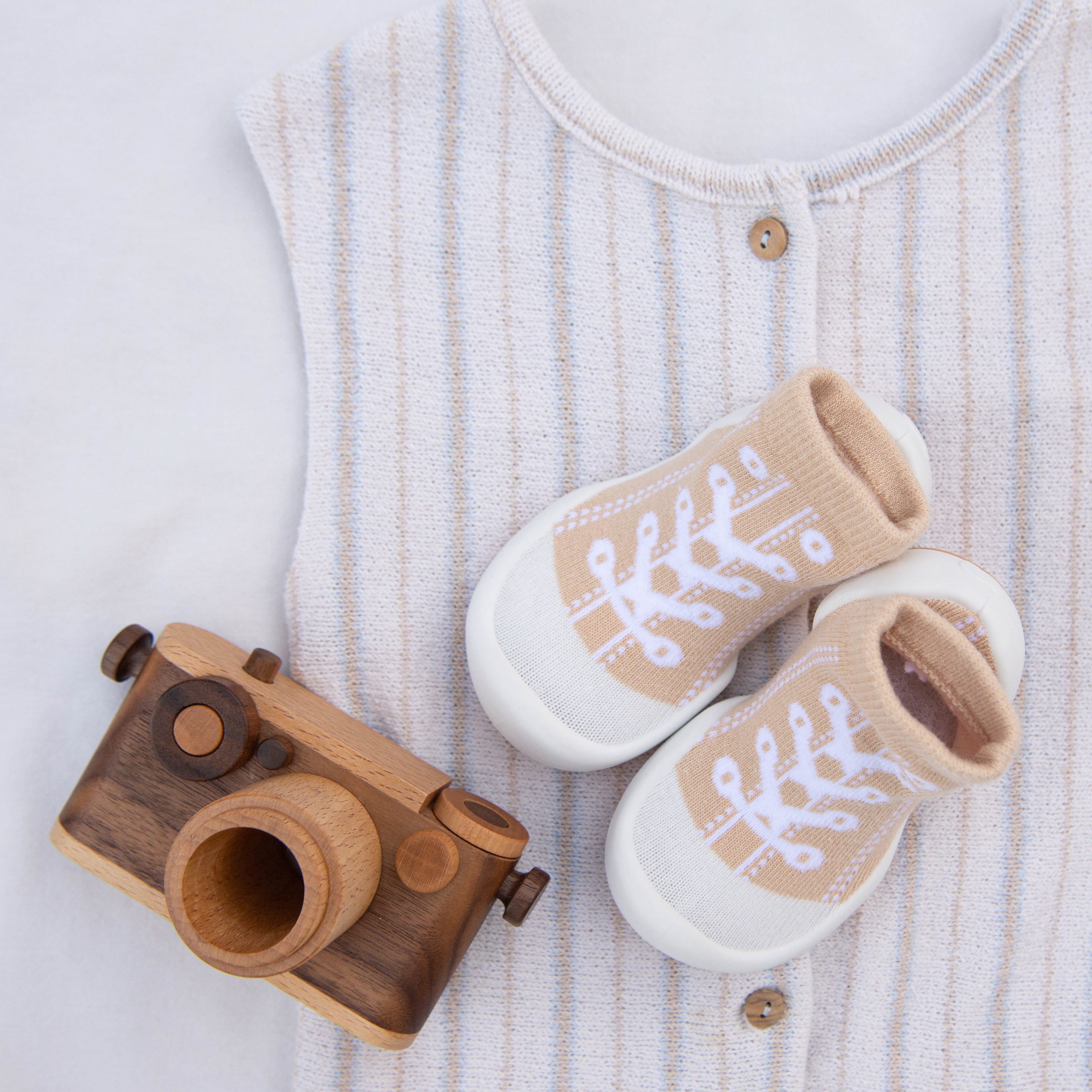 Wooden toy camera, baby's outfit, and beige baby booties.