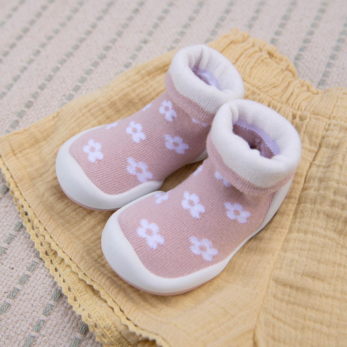 Pair of pink and white baby shoes on yellow fabric.
