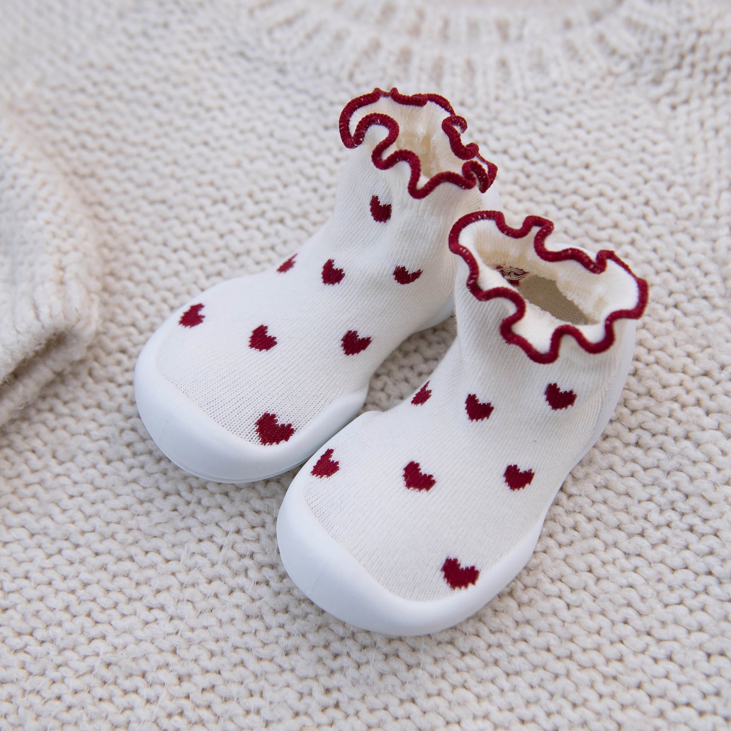 White socks with red hearts and ruffled edges on a textured beige surface