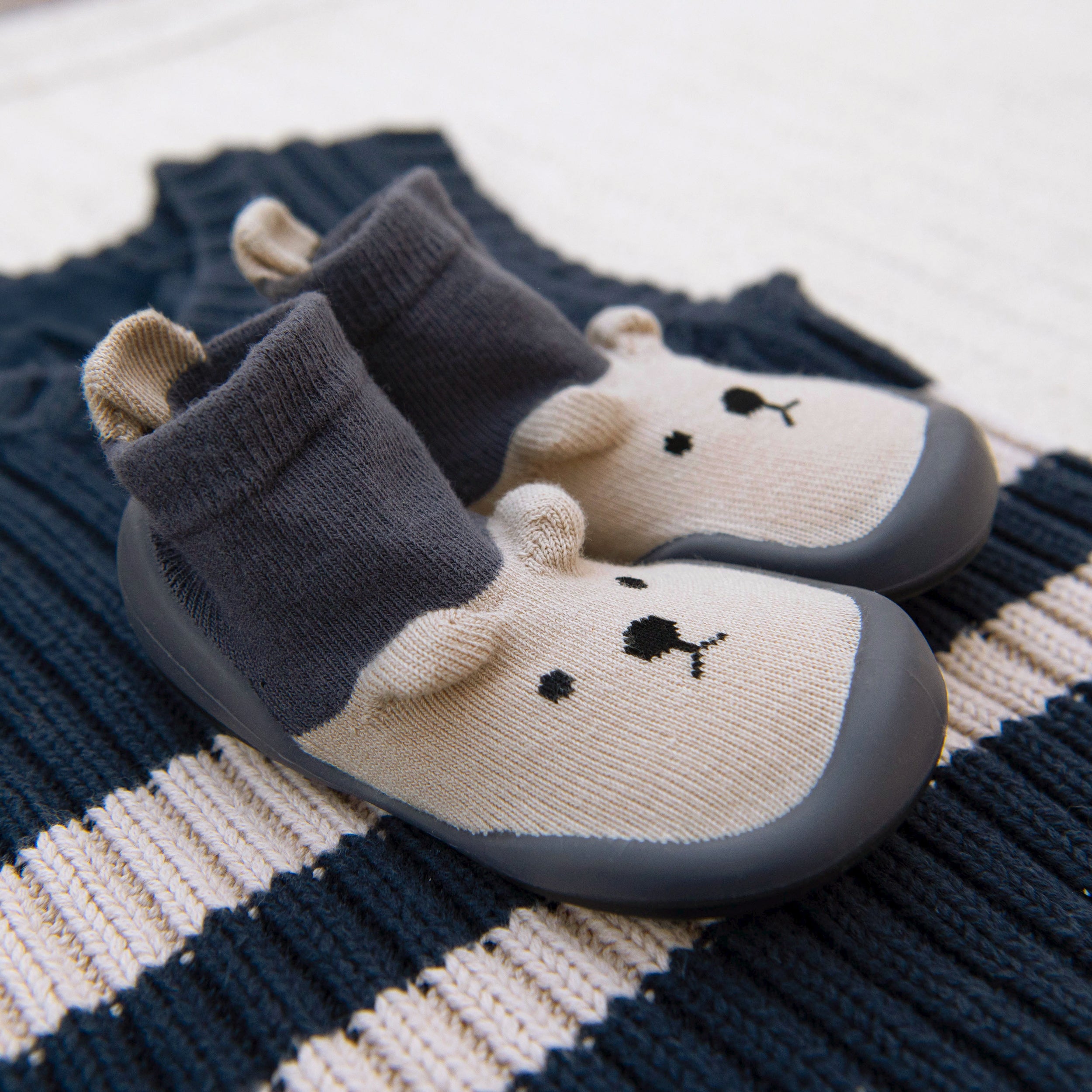Pair of bear-shaped socks with dark gray soles on a striped fabric background