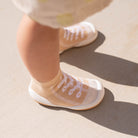 Close-up of a baby's feet in tan and white sock-shoes on concrete in sunlight.