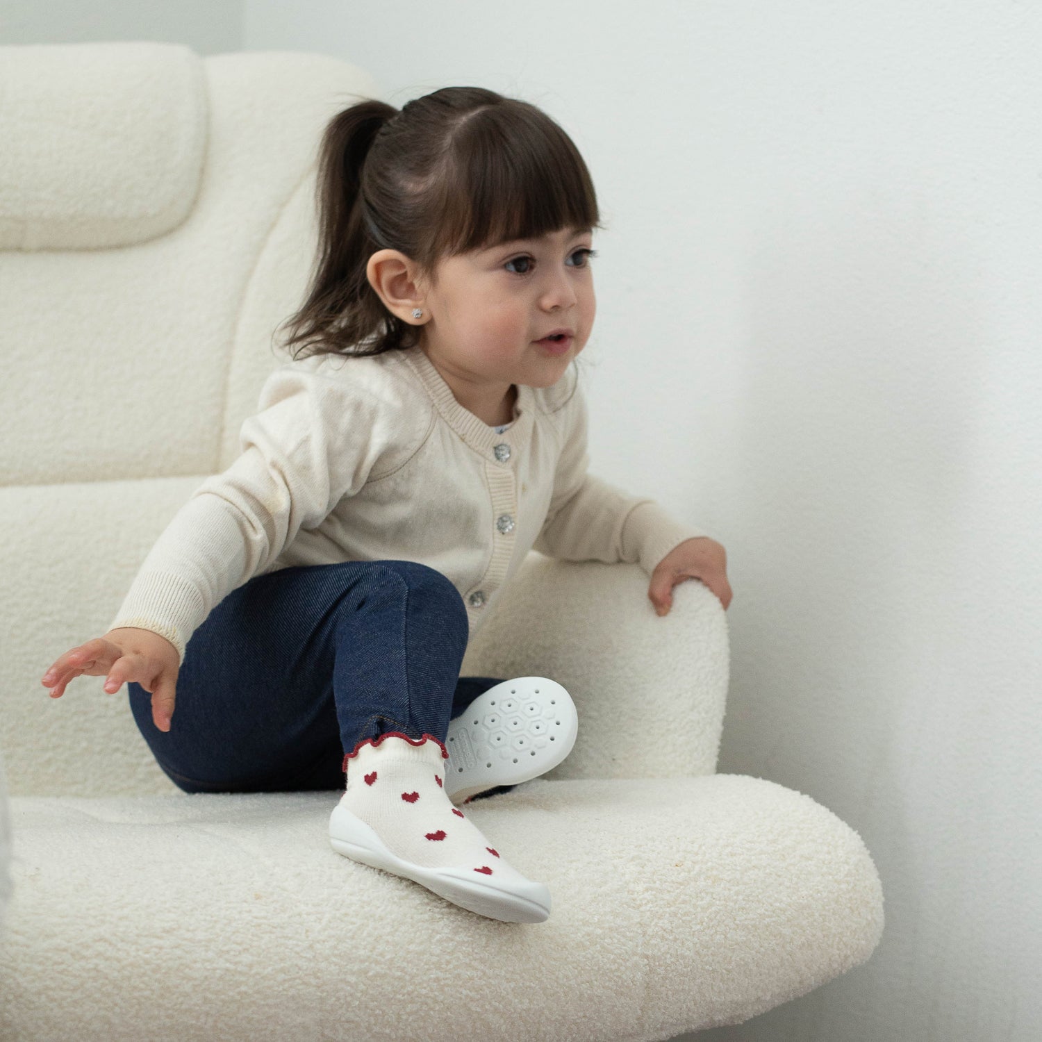 Child sitting on a white chair wearing white shoes with red hearts