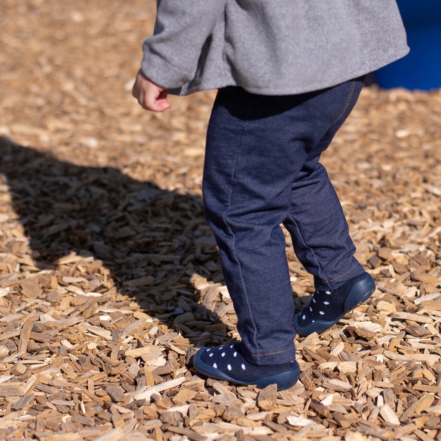 Child wearing navy shoes with white polka dots on a wooden ground