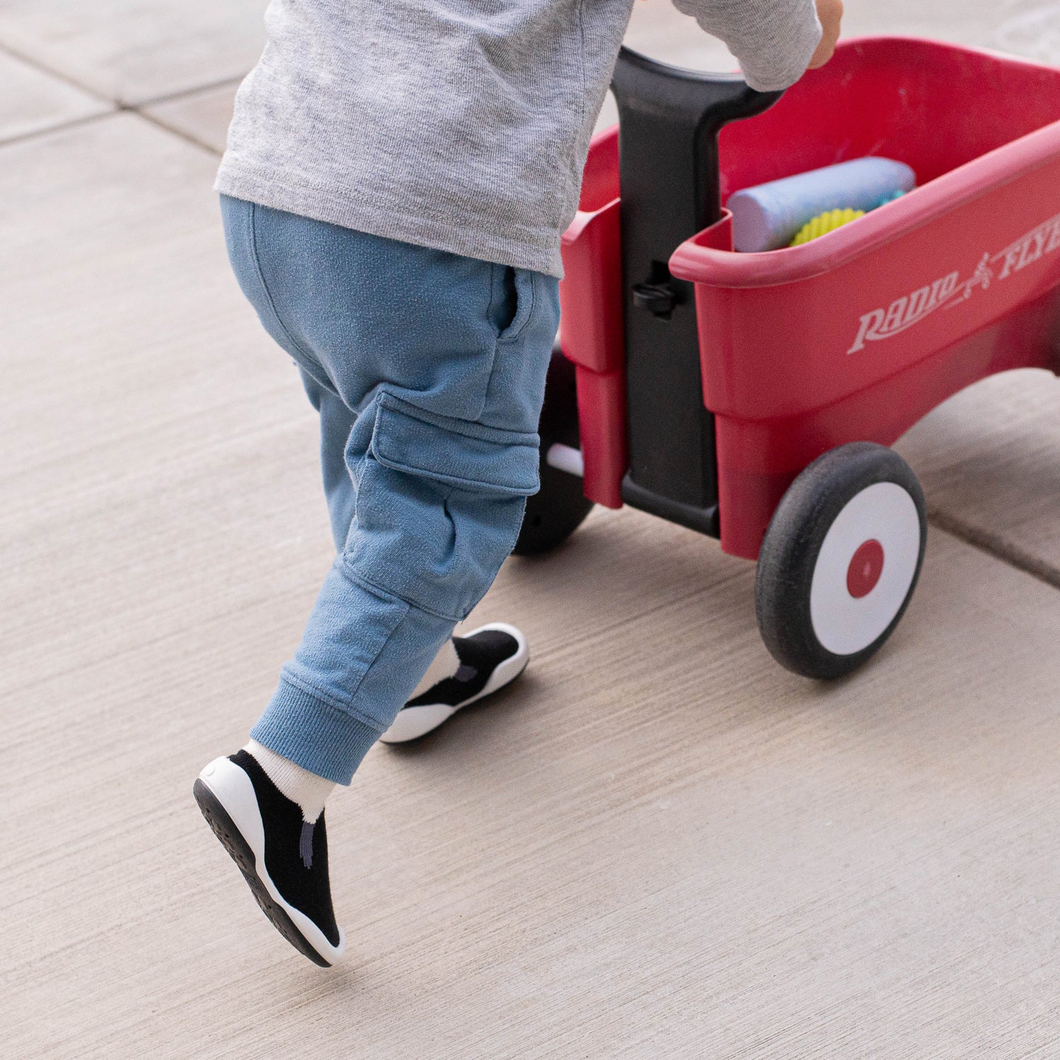 Child pushing a red Radio Flyz toy wagon on a tiled floor