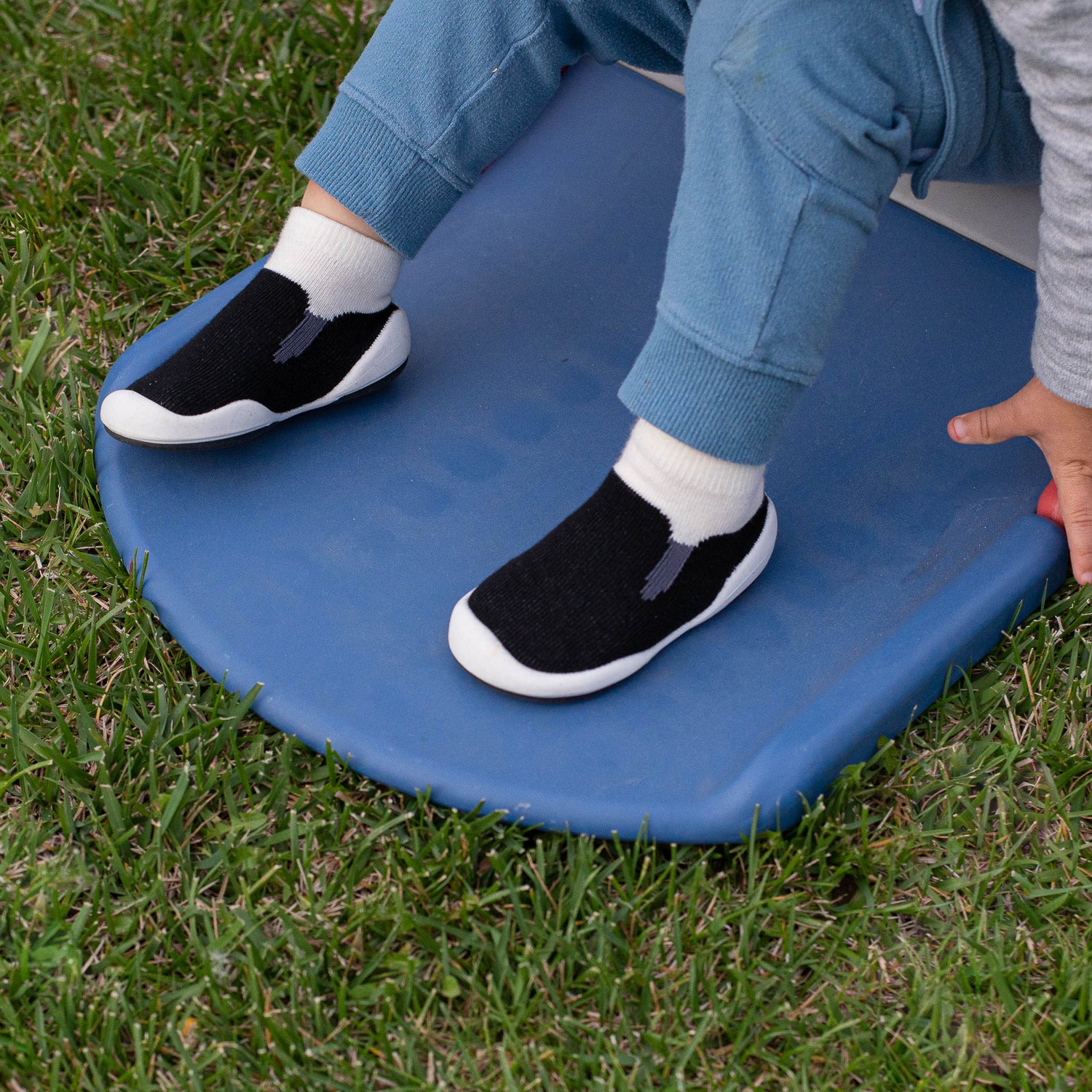 Person wearing black shoes with white socks on a blue mat outdoors.