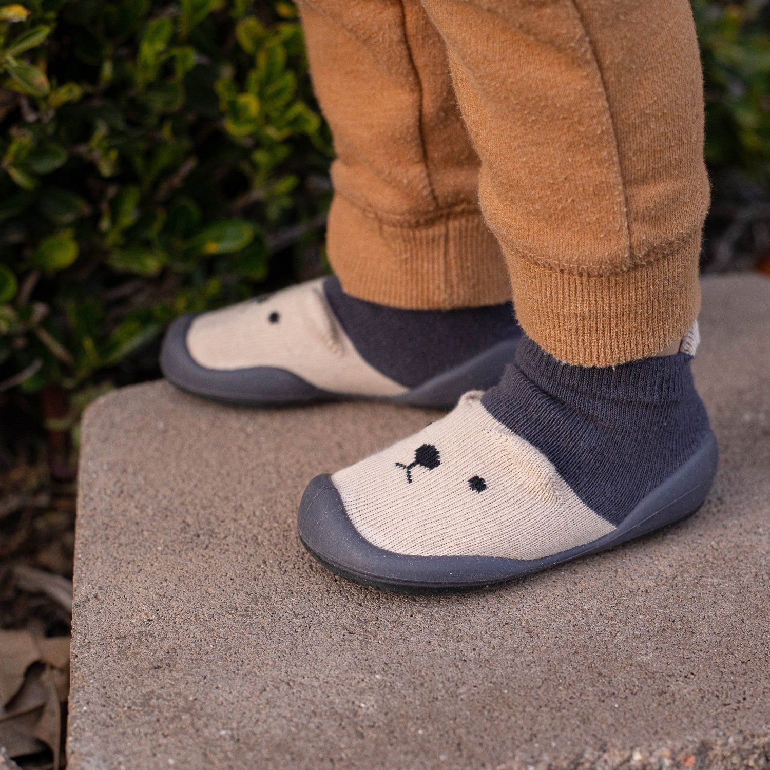 Children's shoes with a floral design worn by a child on a stone surface.