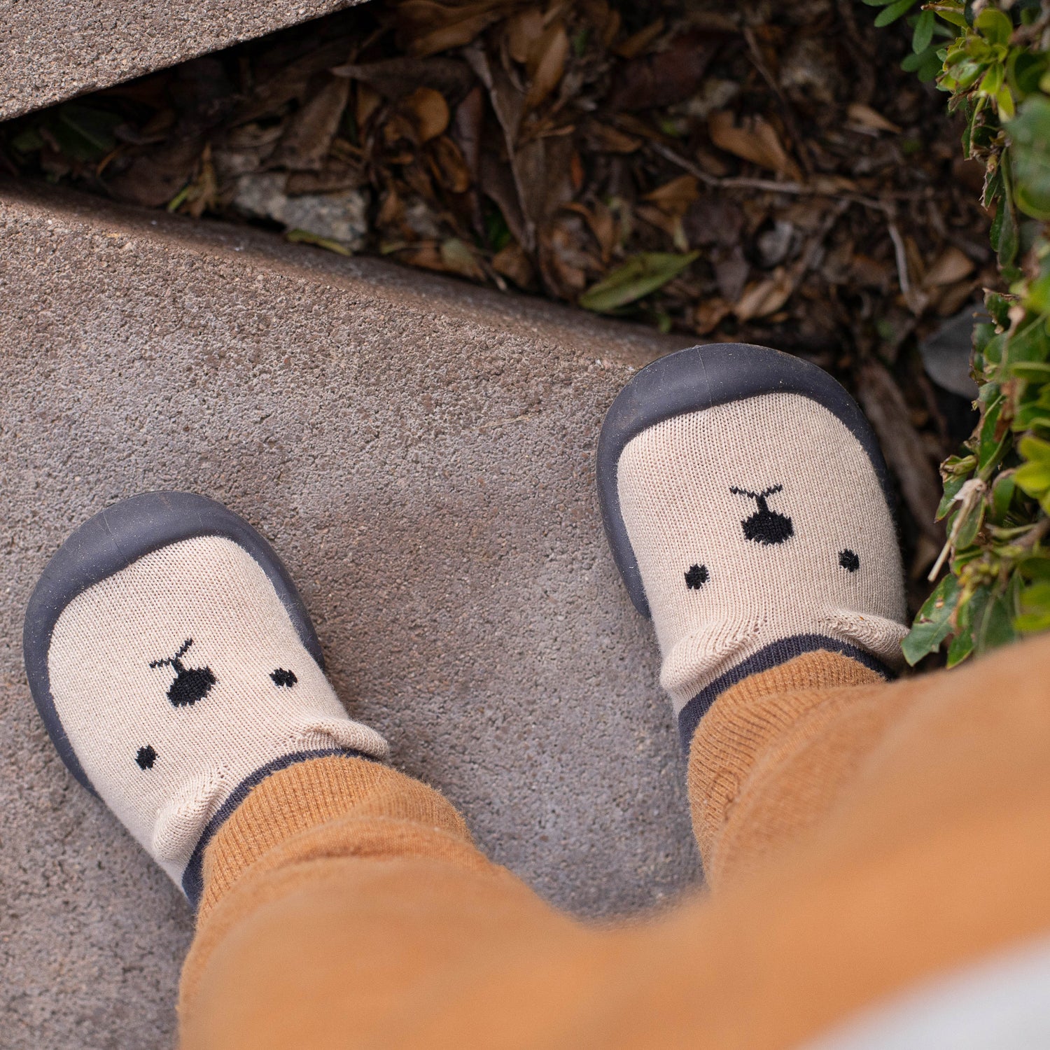 Baby's feet wearing white socks with black details on a concrete surface.