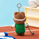 Rear view of a brown plush bear keychain with a white headband, wearing a green vest and holding a golf club on a running track.