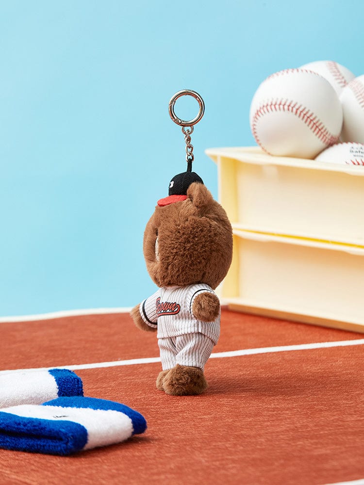 Brown teddy bear keychain, baseball uniform, baseball field setting.