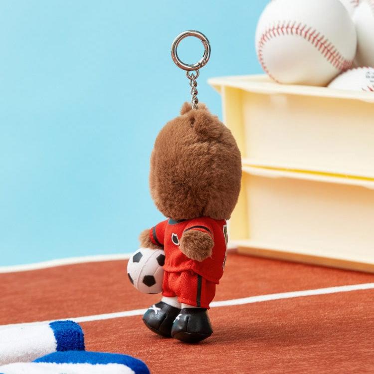 A brown, plush bear keychain dressed in a red soccer uniform holding a soccer ball.