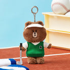 Brown bear keychain toy, wearing a white visor and green sweater with a "B" logo, holding a golf club.