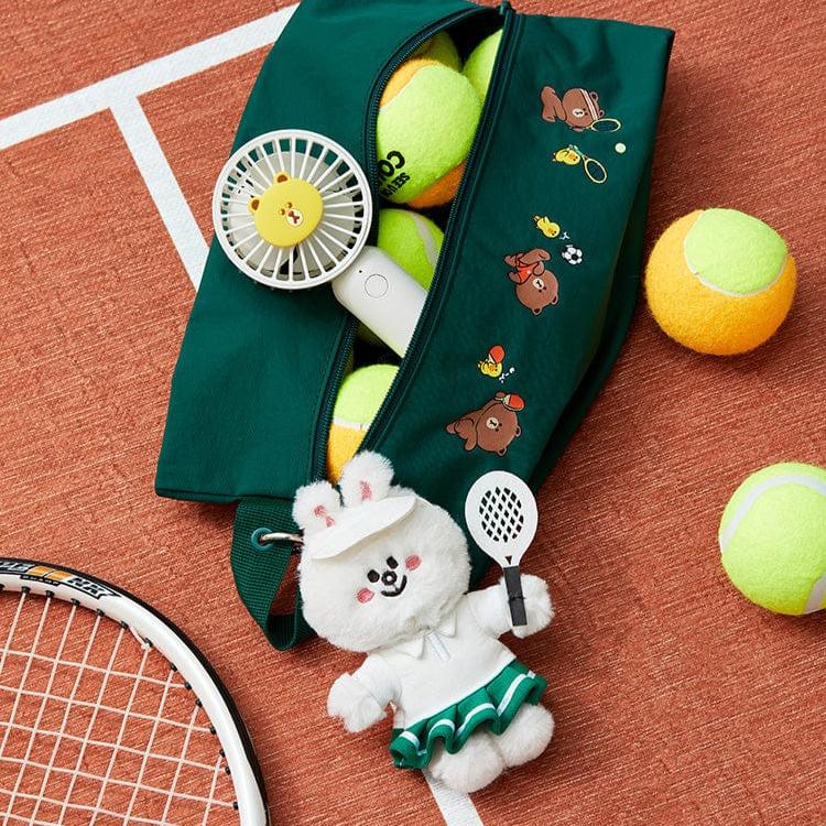 A tennis-themed product shot shows a green tennis bag with cartoon bear decorations filled with tennis balls, a white portable fan, and a white charging device. Next to the bag is a fluffy white bunny doll dressed in a tennis outfit and holding a miniature tennis racket. A tennis racket is partially visible on the left side of the frame, all set against the backdrop of a tennis court.