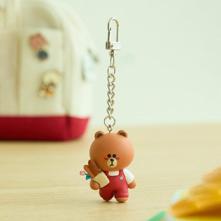 Cartoon bear keychain holding flowers, wearing red overalls.