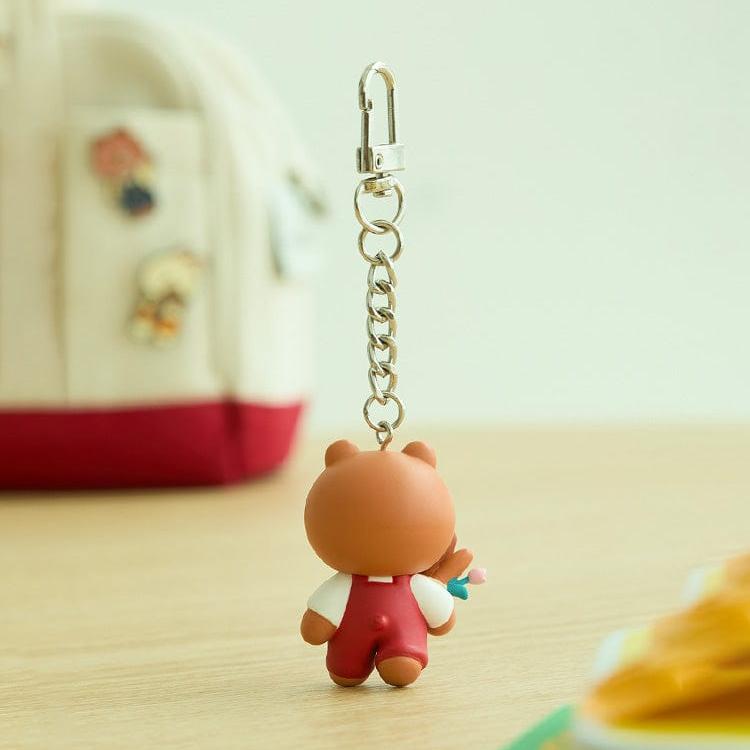 A bear keychain in red overalls with flowers.