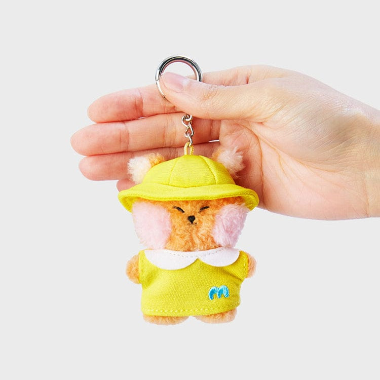 Hand holding plush animal keychain toy wearing yellow hat and shirt.