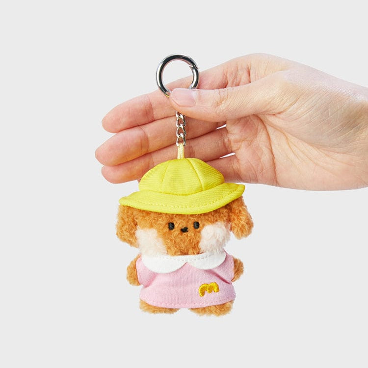 A plush dog keychain with a yellow hat and pink dress held in a hand.