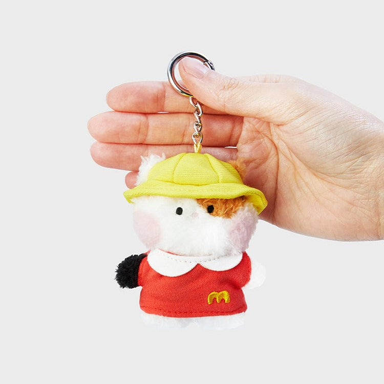 A hand holding a stuffed animal keychain with a yellow hat and a red shirt with a yellow "M" logo.