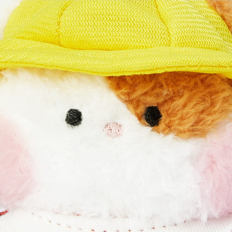 Close-up of a stuffed animal with a yellow cap, pink cheeks, black eyes, and a pink nose.