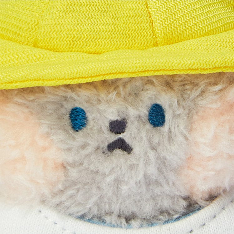 Close-up of a plush toy wearing a yellow hoodie, showcasing a fluffy grey face with blue eyes and a black nose.