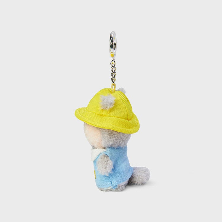Side view of a small, gray, stuffed animal wearing a yellow hat and blue shirt with a metal keychain clasp on top against a light gray background.