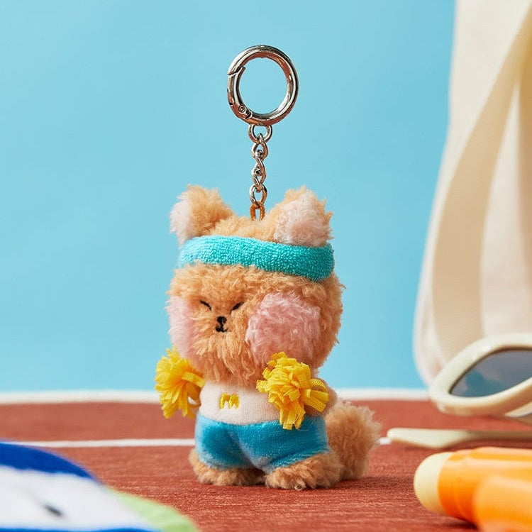 Stuffed animal keychain, light brown fur, turquoise headband, pink cheeks, blue and white outfit with yellow pom-poms.