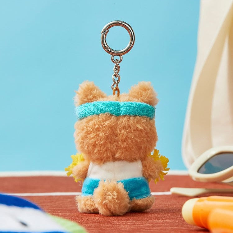 Rear view of a plush bear keychain wearing a blue headband, a white and blue outfit, and holding yellow pom-poms.