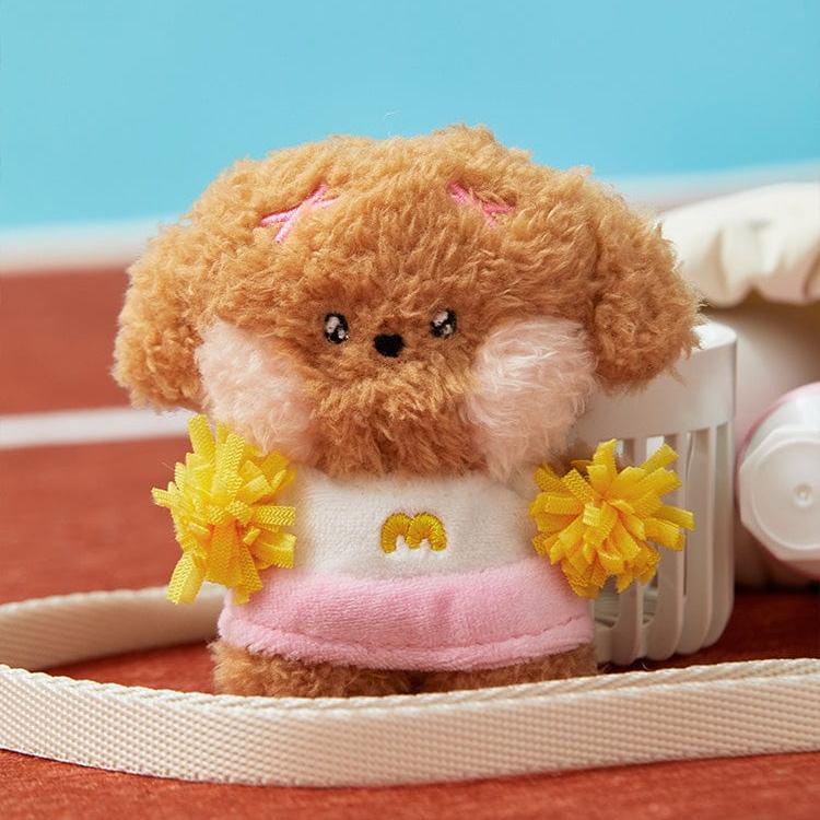 Brown plush toy dog dressed as a cheerleader with yellow pom-poms, a pink skirt, and a white top with a yellow "M".