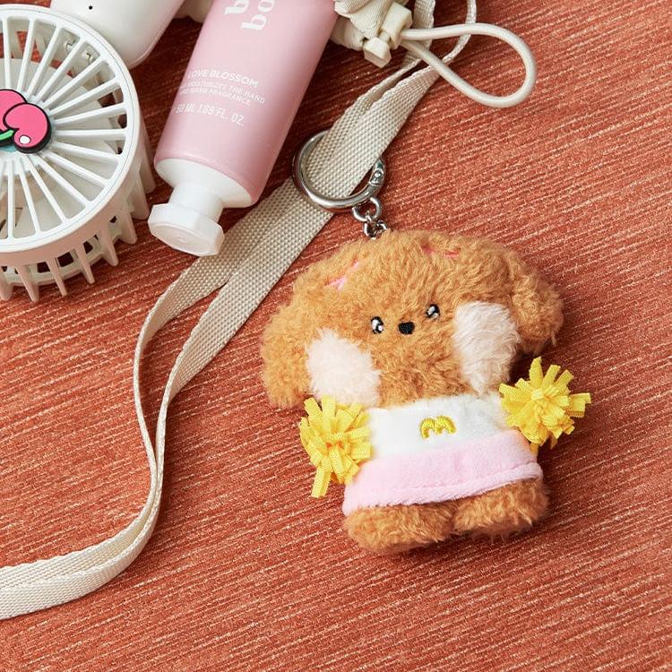 A fuzzy brown dog keychain with a pink and white dress and yellow pom-poms.