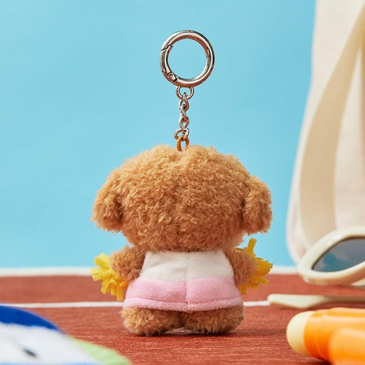 Rear view of a fluffy brown dog keychain with a pink skirt and white top, holding yellow pom-poms.