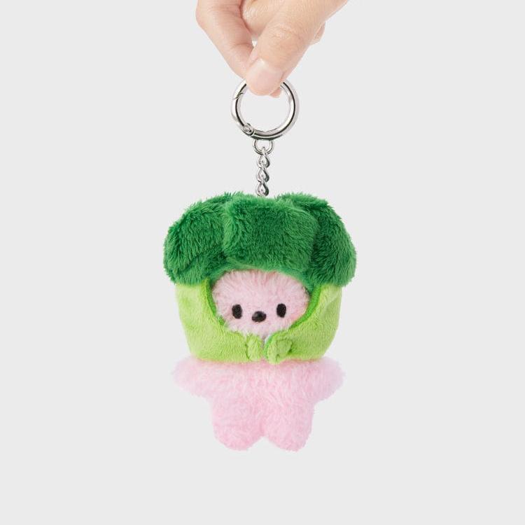 Hand holding a plush toy keychain. Pink figure with a green broccoli hat and body.