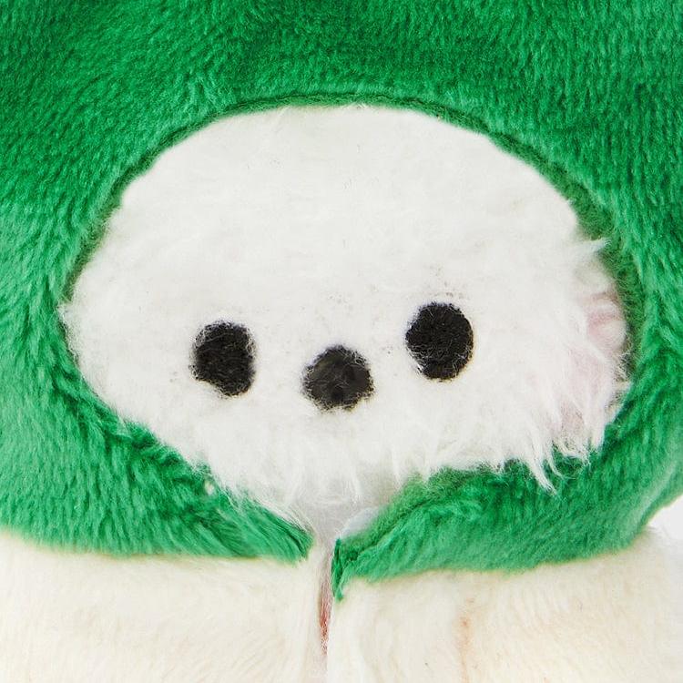 Close-up of a white stuffed animal with three black dots on its face, wearing a fuzzy green hood.