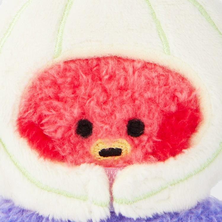 Close-up of a plush cartoon character wearing a hooded jacket. The character has a red face, black eyes, and a yellow mouth. The hood is white and lined with light green trim. The base of the plush is purple.