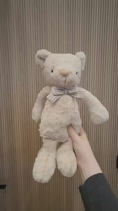 A hand holding a beige teddy bear with a striped bow tie.