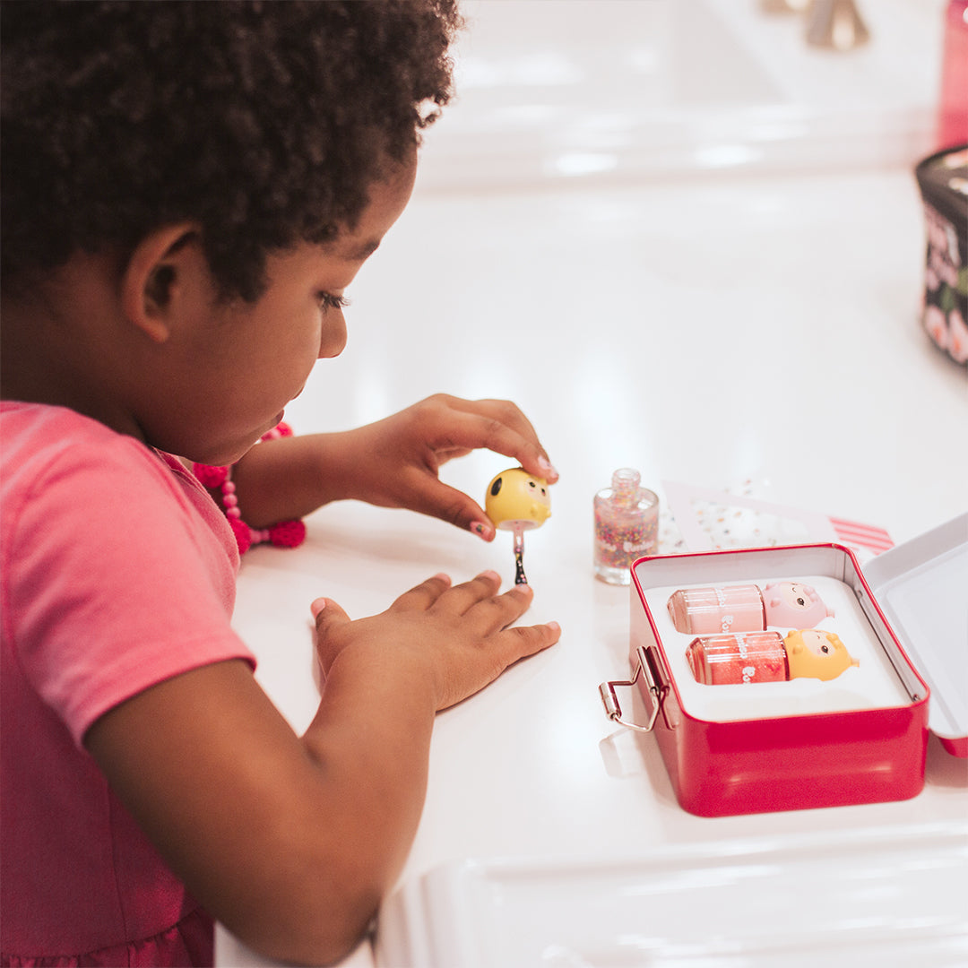 A young Black girl in a pink dress playing with animal-shaped nail polish bottles on a white table.