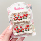 Two crocheted beige hair clips embroidered with red and yellow flowers, displayed on a floral-patterned product card.
