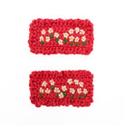 Two red knitted rectangles, each embroidered with daisies, arranged on a white background.