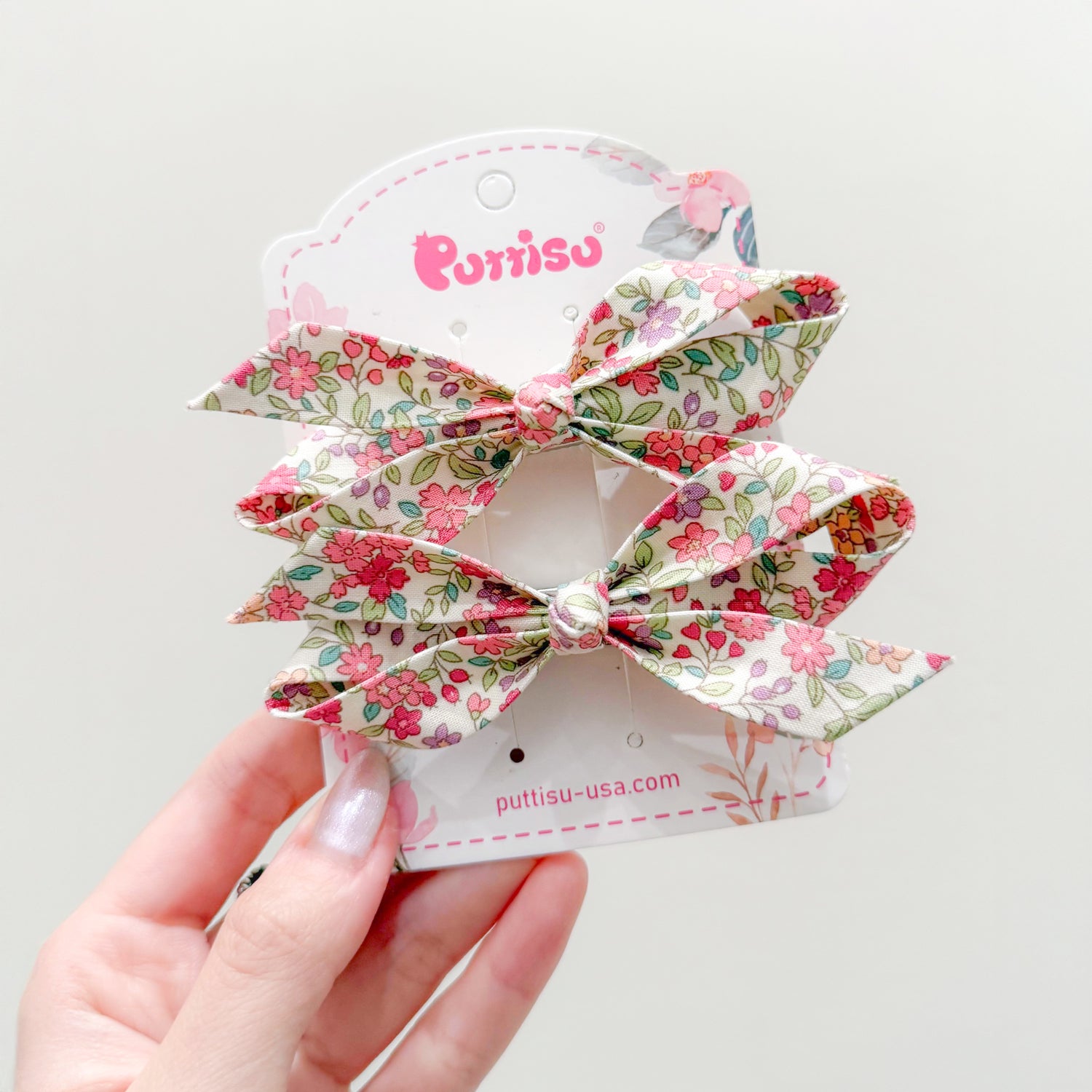 Two floral patterned hair bows held by a hand.