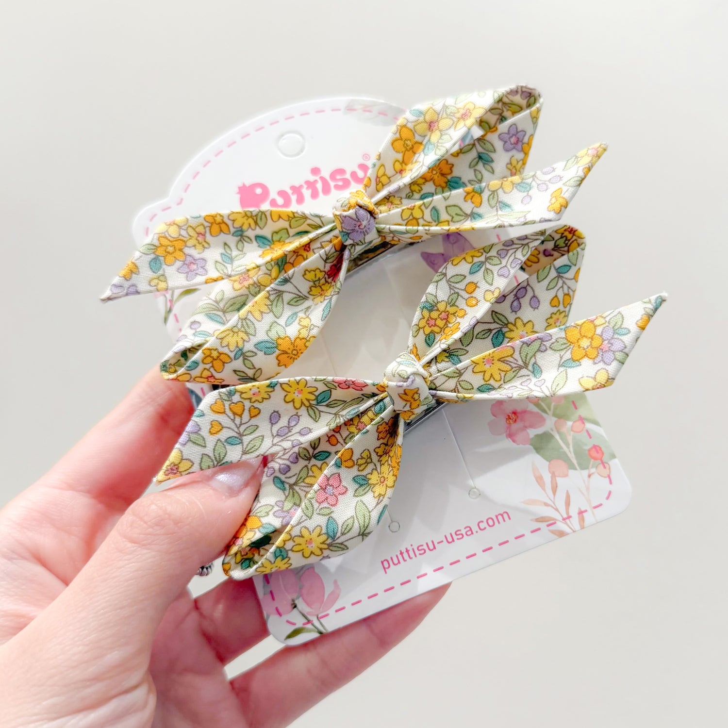 Floral hair bows on a white card held in a hand.