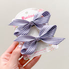 Two purple and white gingham bows on a product card being held by a hand.