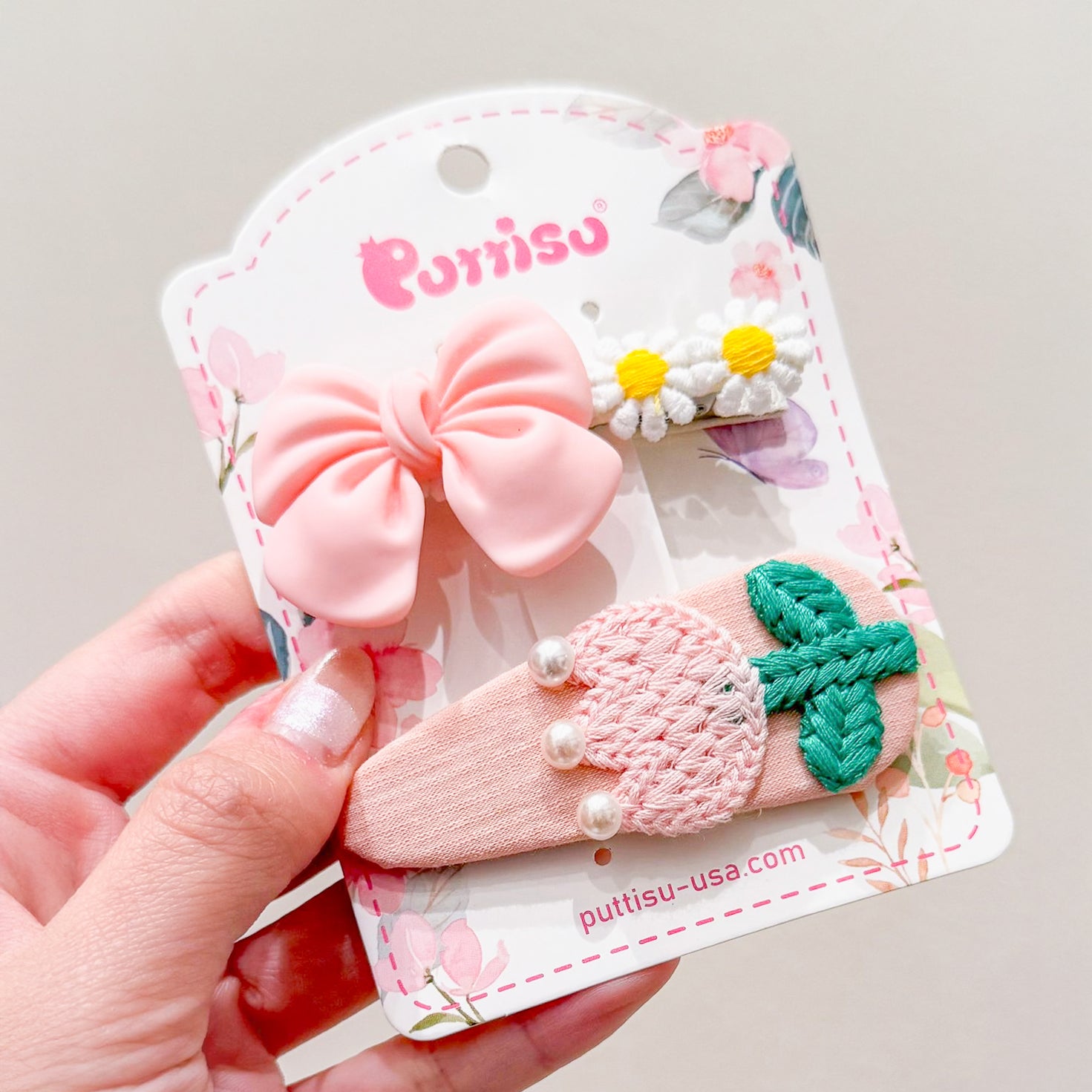 Three hair clips on a decorative card: pink bow, white daisies, and a pink embroidered design with green leaves and pearls.