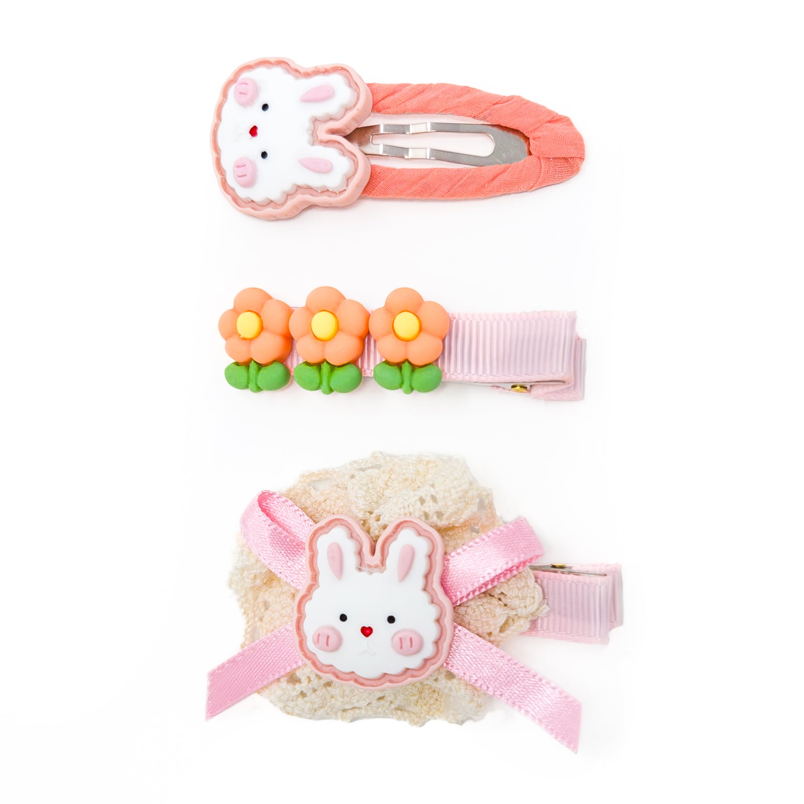Three hair clips: a bunny on orange fabric, three flowers on pink ribbon, and a bunny on lace and pink ribbon.
