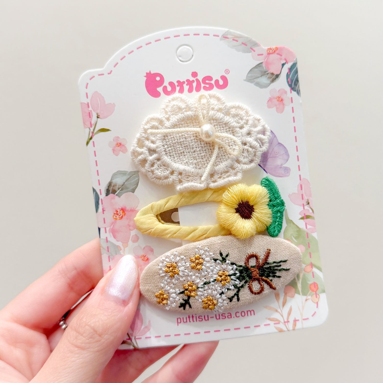 Three embroidered hair clips on a floral-patterned card held by a hand.