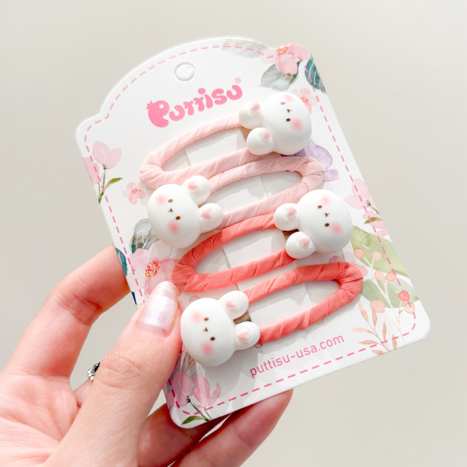 Close-up of a hand holding a card of pastel bunny hair clips.