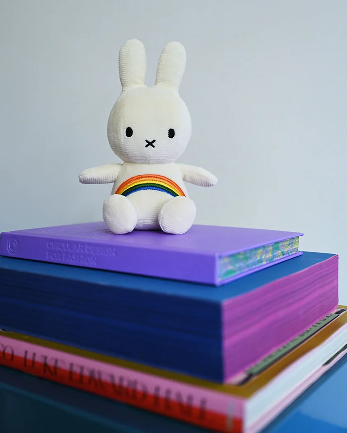 Stuffed bunny sitting on a stack of colorful books.