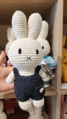 Crocheted white Miffy doll wearing blue overalls.