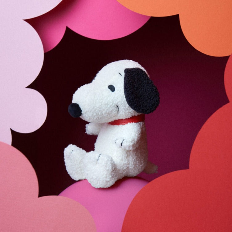 A plush white Snoopy toy wearing a red collar, sitting amidst pink and red paper cutouts.
